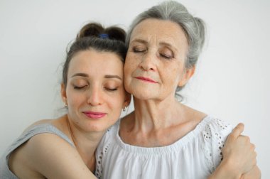Mutlu kıdemli anne yetişkin kızına sarılıyor, kadınlar birlikte gülüyor, farklı nesillerden gelen samimi aile beyaz arka planda eğleniyor.