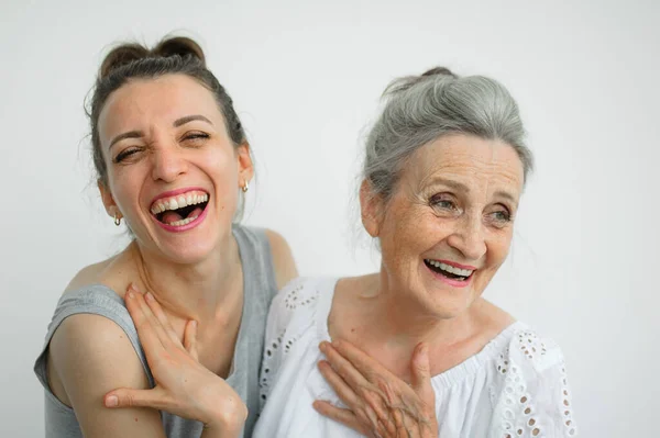 Šťastná starší matka objímá svou dospělou dceru, ženy se spolu smějí, upřímná rodina různých věkových generací se baví na bílém pozadí — Stock fotografie