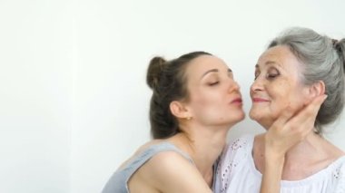 Mutlu kıdemli anne yetişkin kızına sarılıyor, kadınlar birlikte gülüyor, farklı nesillerden gelen samimi aile beyaz arka planda eğleniyor.