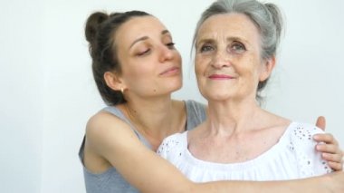 Yetişkin kız, büyük annesine sarılıyor, kadınlar birlikte gülüyor, farklı nesillerden gelen samimi aile beyaz arka planda eğleniyor.