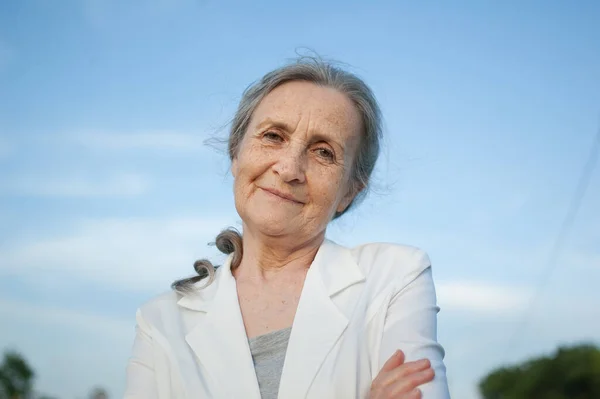 Portret van oudere vrouw met grijs haar en gezicht met rimpels in witte jas en ontspannen in het park tijdens de zonnige dag — Stockfoto