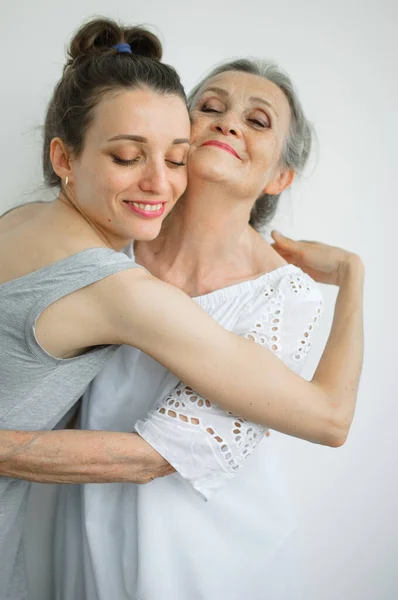 Šťastná starší matka objímá svou dospělou dceru, ženy se spolu smějí, upřímná rodina různých věkových generací se baví na bílém pozadí — Stock fotografie
