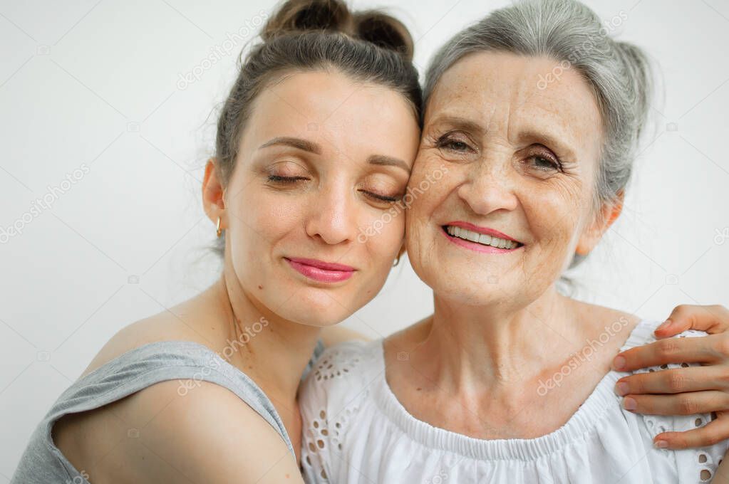 Happy senior mother is hugging her adult daughter, the women are laughing together, sincere family of different age generations having fun on white background