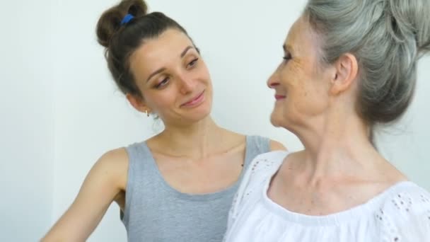 Hija adulta está abrazando a su madre mayor, las mujeres se ríen juntas, familia sincera de diferentes generaciones de edad que se divierten en el fondo blanco — Vídeo de stock