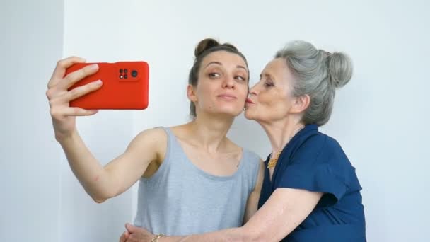 Fille adulte et maman aînée prennent une photo autoportrait, selfie sur smartphone rouge ensemble, retraite heureuse, concepts de la fête des mères. — Video