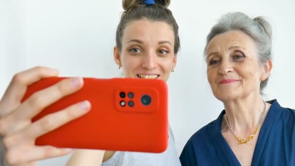 Filha adulta e mãe sênior estão tirando foto de auto-retrato, selfie no smartphone vermelho juntos, aposentadoria feliz, conceitos do dia das mães. — Vídeo de Stock