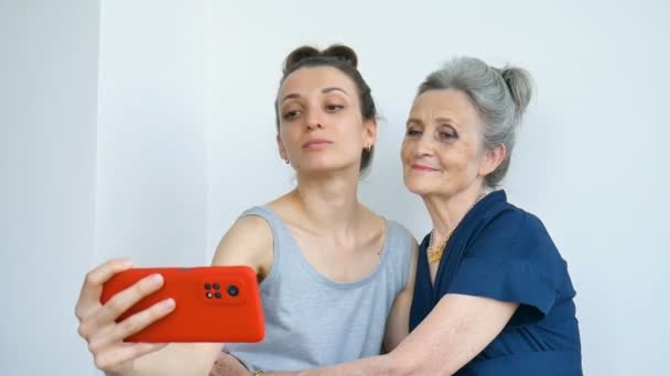 Vuxen dotter och äldre mamma tar självporträtt bild, selfie på röd smartphone tillsammans, glad pension, mödrar dag koncept. — Stockvideo