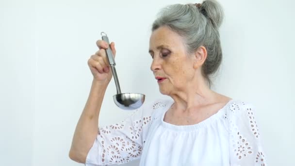 Érzelmi idős nő ezüst hajjal tartja fém merőkanál vagy kanál fehér háttér, boldog nyugdíjazás, anyák napi fogalmak. — Stock videók