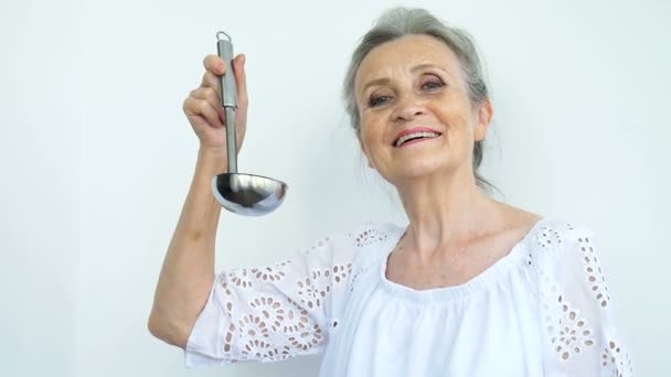 Emotional senior woman with silver hair is holding metal ladle or scoop on white background, happy retirement, mothers day concepts. — Stock Video