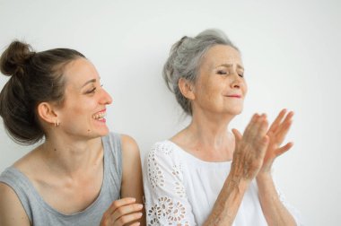 Mutlu kıdemli anne yetişkin kızına sarılıyor, kadınlar birlikte gülüyor, farklı nesillerden gelen samimi aile beyaz arka planda eğleniyor.