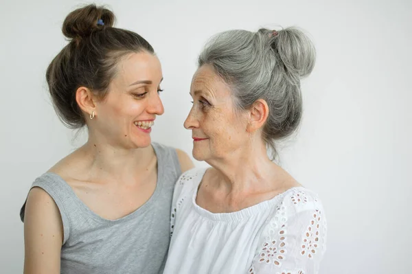 Happy senior mother is hugging her adult daughter, the women are laughing together, sincere family of different age generations having fun on white background, mothers day. — Stock Photo, Image
