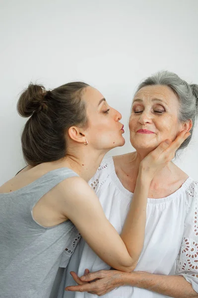 Feliz madre mayor está abrazando a su hija adulta, las mujeres se ríen juntas, familia sincera de diferentes generaciones de edad que se divierten en el fondo blanco, día de las madres. —  Fotos de Stock