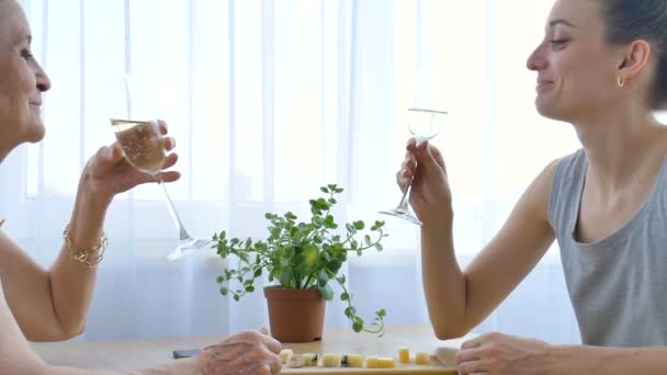 Retrato femenino de la hija adulta y la madre mayor hablando y bebiendo champán en casa sentado en la mesa, jubilación feliz, conceptos del día de las madres, adicción al alcohol — Vídeos de Stock