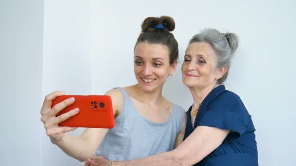 Filha adulta e mãe sênior estão tirando foto de auto-retrato, selfie no smartphone vermelho juntos, aposentadoria feliz, conceitos do dia das mães. — Vídeo de Stock