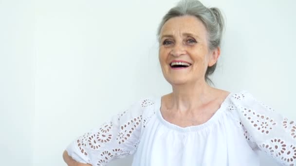 Vacker gammal mormor med grått hår och ansikte med rynkor tittar på kameran med leende på vit bakgrund, mödrar dag, glad pension — Stockvideo