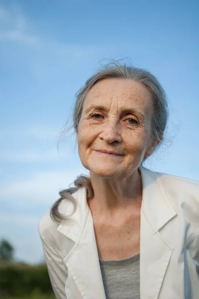 Portret van oudere vrouw met grijs haar en gezicht met rimpels in witte jas en ontspannen in het park bij zonnig weer, Moederdag — Stockfoto