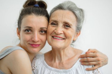 Mutlu kıdemli anne, yetişkin kızına sarılıyor. Kadınlar birlikte gülüyor. Farklı nesillerden dürüst bir aile beyaz arka planda eğleniyor..
