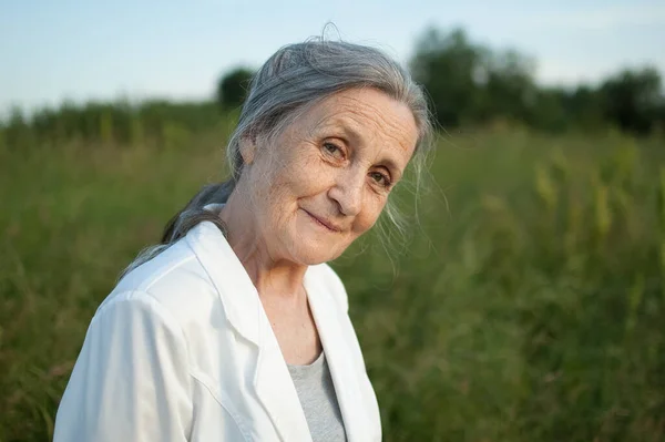 Retrato de mujer mayor con el pelo gris y la cara con arrugas con chaqueta blanca y relajarse en el parque durante el tiempo soleado, día de las madres — Foto de Stock