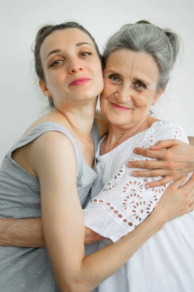 Feliz madre mayor está abrazando a su hija adulta, las mujeres se ríen juntas, familia sincera de diferentes generaciones de edad que se divierten en el fondo blanco, día de las madres. —  Fotos de Stock