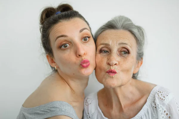 Feliz madre mayor está abrazando a su hija adulta, las mujeres se ríen juntas, familia sincera de diferentes generaciones de edad que se divierten en el fondo blanco, día de las madres. —  Fotos de Stock