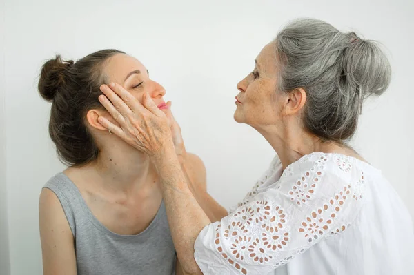 Feliz madre mayor está abrazando a su hija adulta, las mujeres se ríen juntas, familia sincera de diferentes generaciones de edad que se divierten en el fondo blanco —  Fotos de Stock