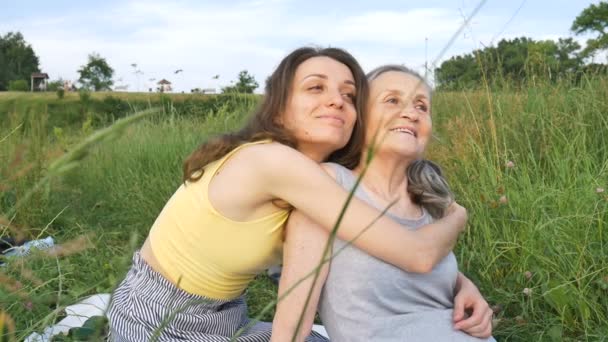 Madre anziana con i capelli grigi con la figlia adulta in giardino che si abbraccia durante il picnic durante la giornata di sole all'aperto, la giornata delle madri — Video Stock