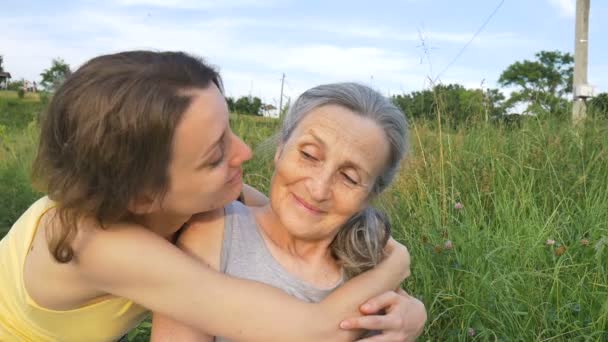 Madre mayor con el pelo gris con su hija adulta en el jardín abrazándose durante el picnic durante el día soleado al aire libre, el día de las madres — Vídeo de stock