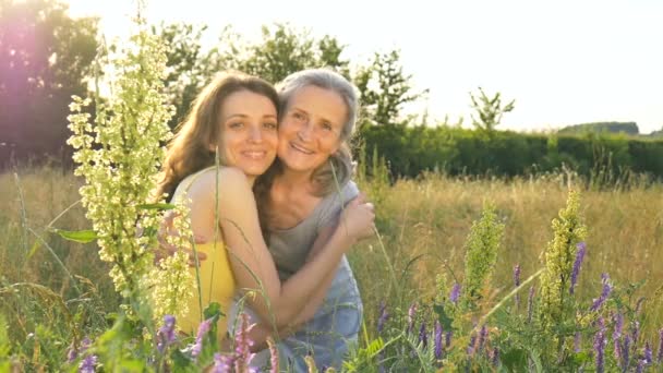 Madre mayor con el pelo gris con su hija adulta mirando a la cámara en el jardín y abrazándose durante el atardecer al aire libre, día de las madres — Vídeo de stock