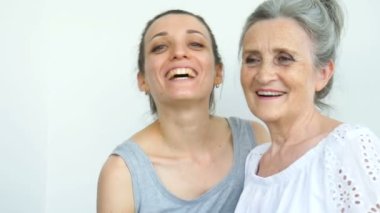 Mutlu kıdemli anne yetişkin kızına sarılıyor, kadınlar birlikte gülüyor, farklı nesillerden gelen samimi aile beyaz arka planda eğleniyor.
