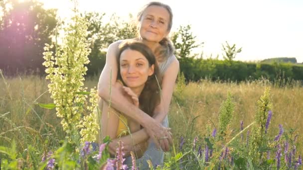 Ältere Mutter mit grauen Haaren mit ihrer erwachsenen Tochter, die im Garten in die Kamera schaut und sich bei Sonnenuntergang im Freien umarmt, Muttertag — Stockvideo