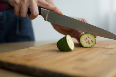 Dişi eller kesilmiş bir tahta üzerinde taze yeşil bir feijoa meyvesi kesiyor. Egzotik meyveler, sağlıklı beslenme konsepti
