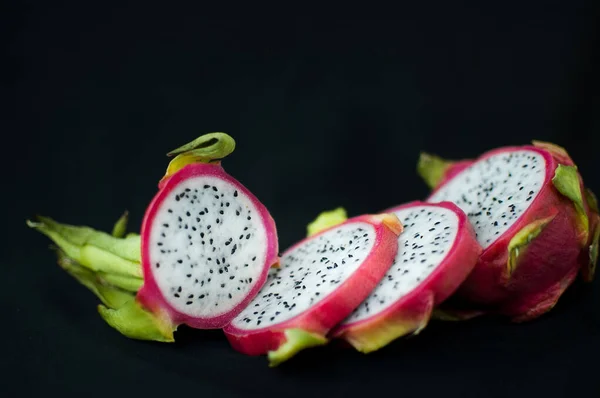 Slices of dragon fruit or pitaya with pink skin and white pulp with seeds on black background. Exotic fruits, healthy eating concept