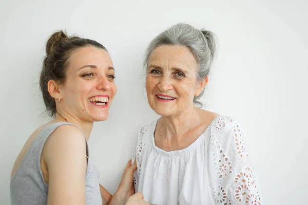 Mutlu kıdemli anne, yetişkin kızına sarılıyor. Kadınlar birlikte gülüyor. Farklı nesillerden dürüst bir aile beyaz arka planda eğleniyor.. — Stok fotoğraf