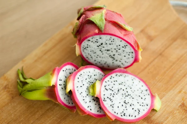 Slices of dragon fruit or pitaya with pink skin and white pulp with black seeds on wooden cut board on the kitchen. Exotic fruits, healthy eating concept