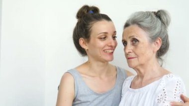 Mutlu kıdemli anne yetişkin kızına sarılıyor, kadınlar birlikte gülüyor, farklı nesillerden gelen samimi aile beyaz arka planda eğleniyor.
