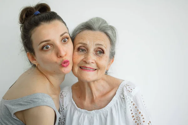 Glückliche Seniorin umarmt ihre erwachsene Tochter, die Frauen lachen zusammen, aufrichtige Familie unterschiedlichen Alters hat Spaß auf weißem Hintergrund, Muttertag. — Stockfoto