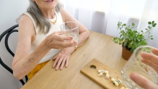 연로 한 어머니가 이야기하고 술을 마시고, 집에서 탁자에 앉아 행복 한 은퇴, 어머니 날 개념, 알코올 중독의 여성 화상 — 비디오
