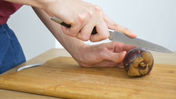 Vrouwelijke handen snijden met mes een verse rijpe mangosteen op een gesneden houten plank. Exotische vruchten, gezond eten concept — Stockvideo