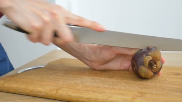 Vrouwelijke handen snijden met mes een verse rijpe mangosteen op een gesneden houten plank. Exotische vruchten, gezond eten concept — Stockvideo