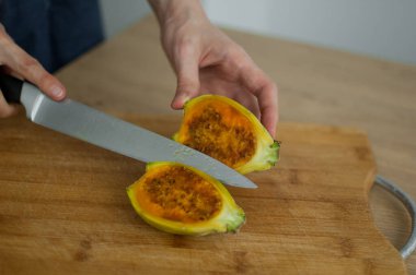 Dişi eller taze olgun bir kaktüs armudunu kesilmiş bir tahta üzerinde kesiyor. Egzotik meyveler, sağlıklı beslenme konsepti.