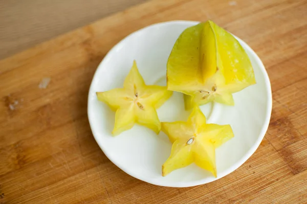 Exotické hvězdicové ovoce nebo averrhoa karamboly na bílém talíři na dřevěné řezací desce. Zdravé jídlo, čerstvé organické hvězdné jablečné ovoce. — Stock fotografie