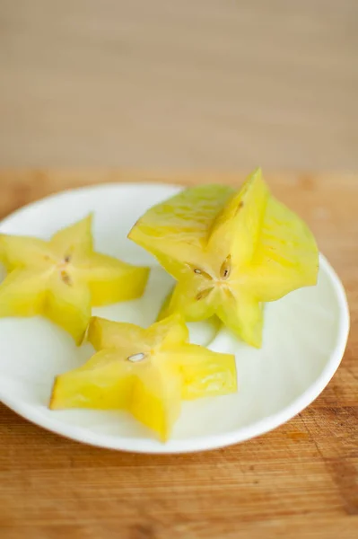 Exotic starfruit or averrhoa carambola on white plate on wooden cut board. Healthy food, fresh organic star apple fruit. — Stock Photo, Image