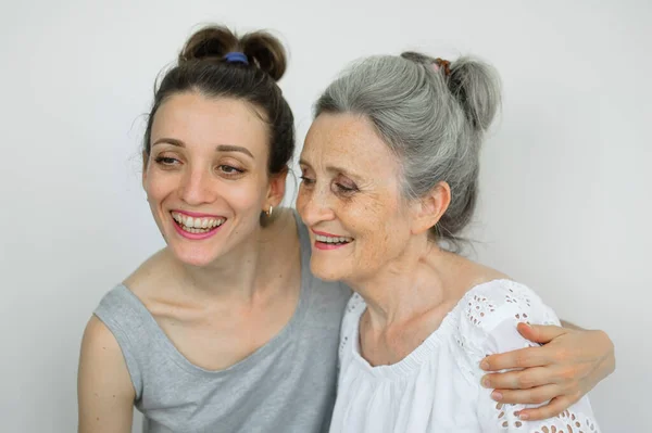 Šťastná starší matka objímá svou dospělou dceru, ženy se spolu smějí, upřímná rodina různých věkových generací se baví na bílém pozadí, Den matek. — Stock fotografie
