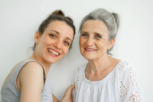 Feliz madre mayor está abrazando a su hija adulta, las mujeres se ríen juntas, familia sincera de diferentes generaciones de edad que se divierten en el fondo blanco, día de las madres. — Foto de Stock