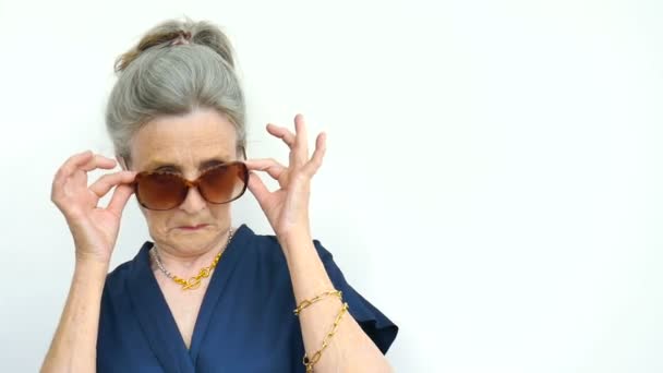 Gyönyörű öreg vicces nagymama ősz haj és az arc ráncok visel napszemüveg fehér háttér, anyák napja, boldog nyugdíjba vonulás — Stock videók