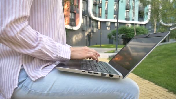 Mujer joven escribiendo en el teclado de la computadora portátil, mujer de negocios utilizando tableta digital fuera en el fondo del edificio moderno, gerente de cuenta trabajando al aire libre, trabajo remoto — Vídeos de Stock