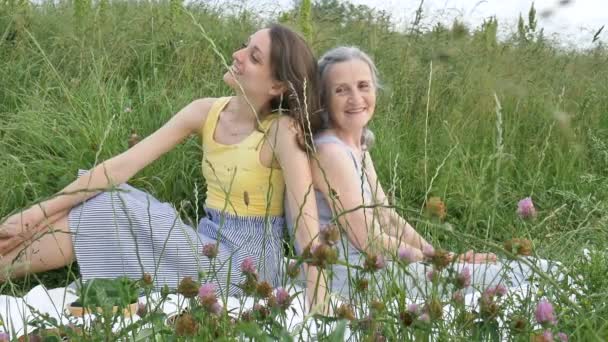 Krásná stará babička s šedivými vlasy a tváří s vráskami leží na bílém koberci se svou dospělou dcerou na zelené trávě během pikniku venku, Den matek, šťastný odchod do důchodu — Stock video