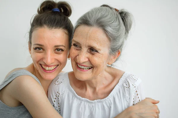 Feliz madre mayor está abrazando a su hija adulta, las mujeres se ríen juntas, familia sincera de diferentes generaciones de edad que se divierten en el fondo blanco, día de las madres. —  Fotos de Stock