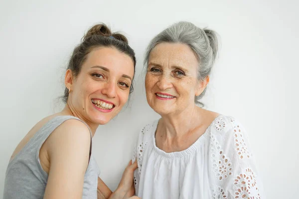 Feliz madre mayor está abrazando a su hija adulta, las mujeres se ríen juntas, familia sincera de diferentes generaciones de edad que se divierten en el fondo blanco, día de las madres. — Foto de Stock