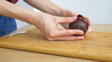 Dişi eller ahşap bir masada taze olgun bir mangosteen tutuyor. Egzotik meyveler, sağlıklı beslenme konsepti
